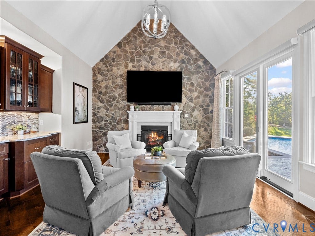 7750 Rock Cress Place, Chesterfield, VA 23120 Vaulted ceiling featuring a stone-faced fireplace with a white mantel, complemented by wood-finish flooring, built-in cabinetry with stone-style backsplash, and glass-paneled exterior doors