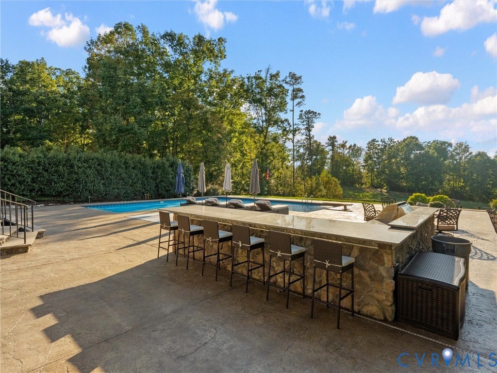 7750 Rock Cress Place, Chesterfield, VA 23120 Outdoor entertainment area featuring a stone-clad wet bar with a solid surface countertop, an in-ground swimming pool, and an expansive stamped concrete patio