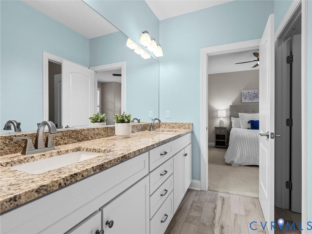 7750 Rock Cress Place, Chesterfield, VA 23120 Dual-sink vanity featuring stone countertops, white shaker-style cabinetry, matte black hardware, a wall-to-wall mirror, and wood-finish flooring