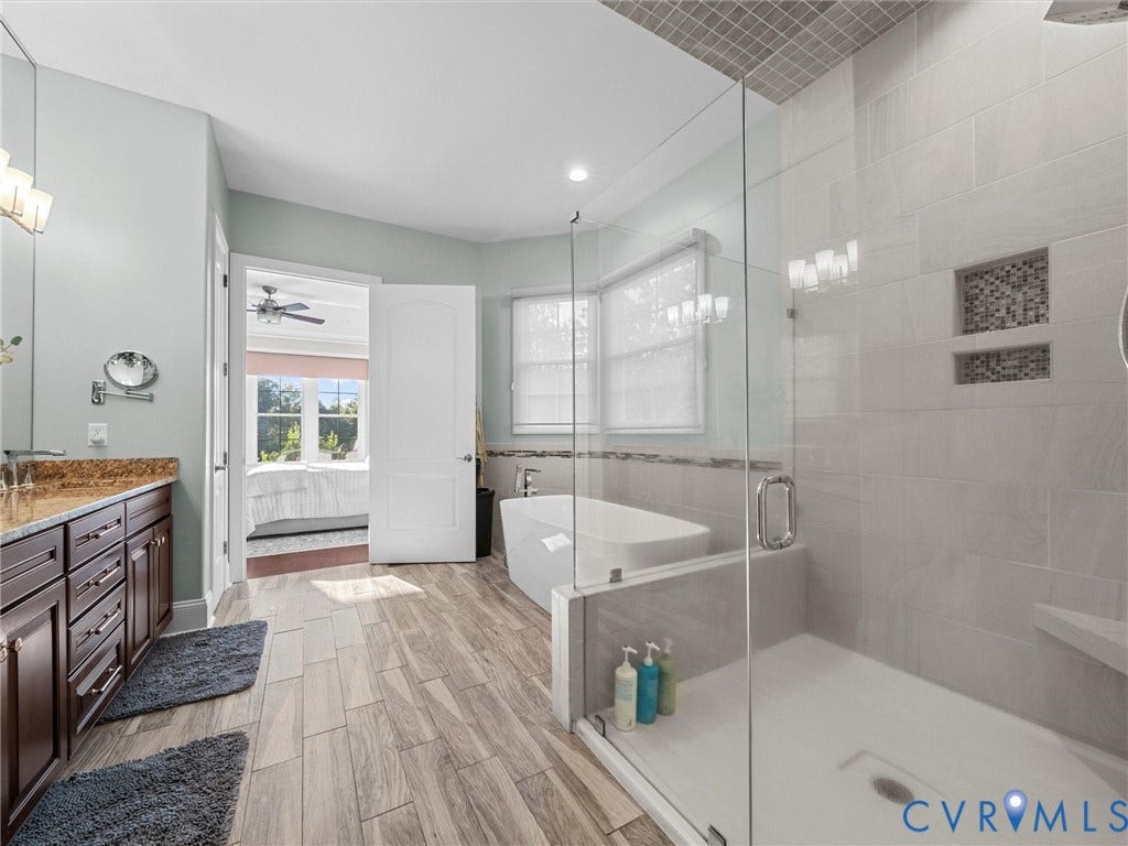 7750 Rock Cress Place, Chesterfield, VA 23120 Bathroom featuring wood-finish tile flooring, a standalone soaking tub, a glass-enclosed walk-in shower with a built-in bench and recessed niche, and dark wood cabinetry with stone-finish countertops