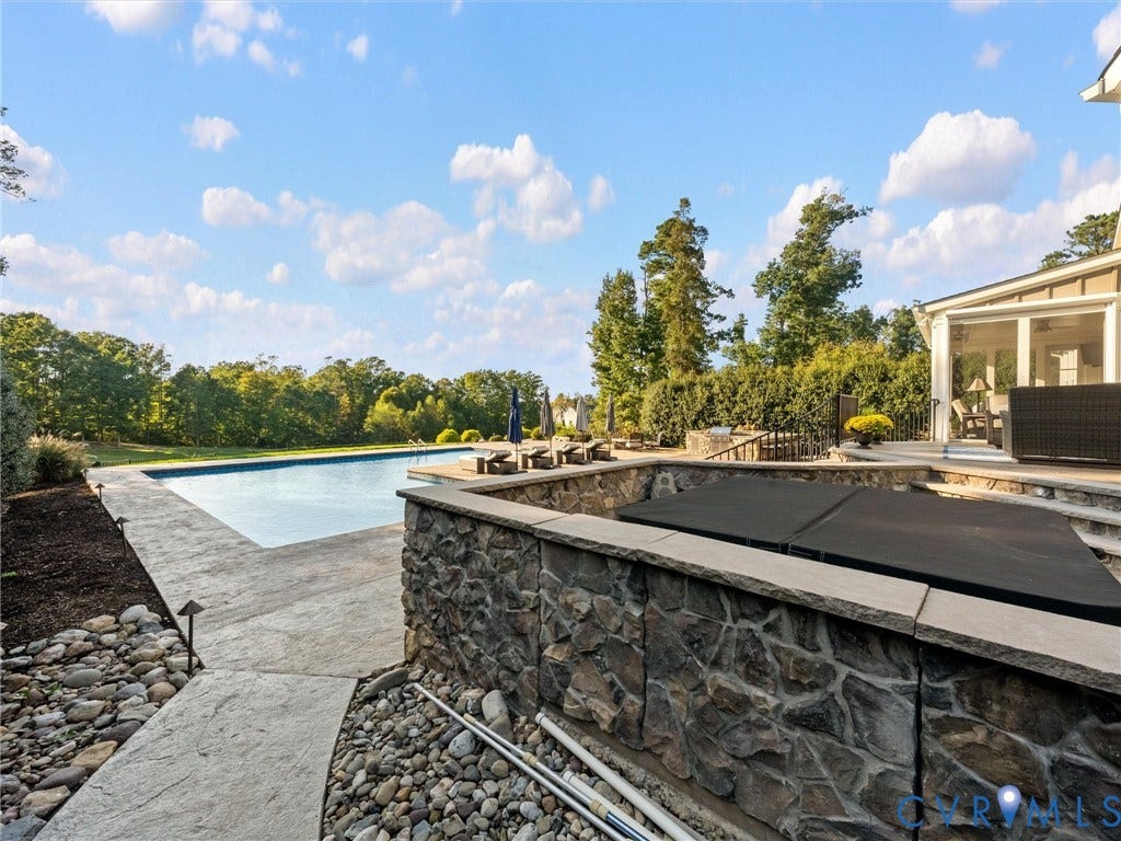 7750 Rock Cress Place, Chesterfield, VA 23120 In-ground swimming pool with stone hardscaping, raised spa featuring natural stone veneer, and stamped concrete decking