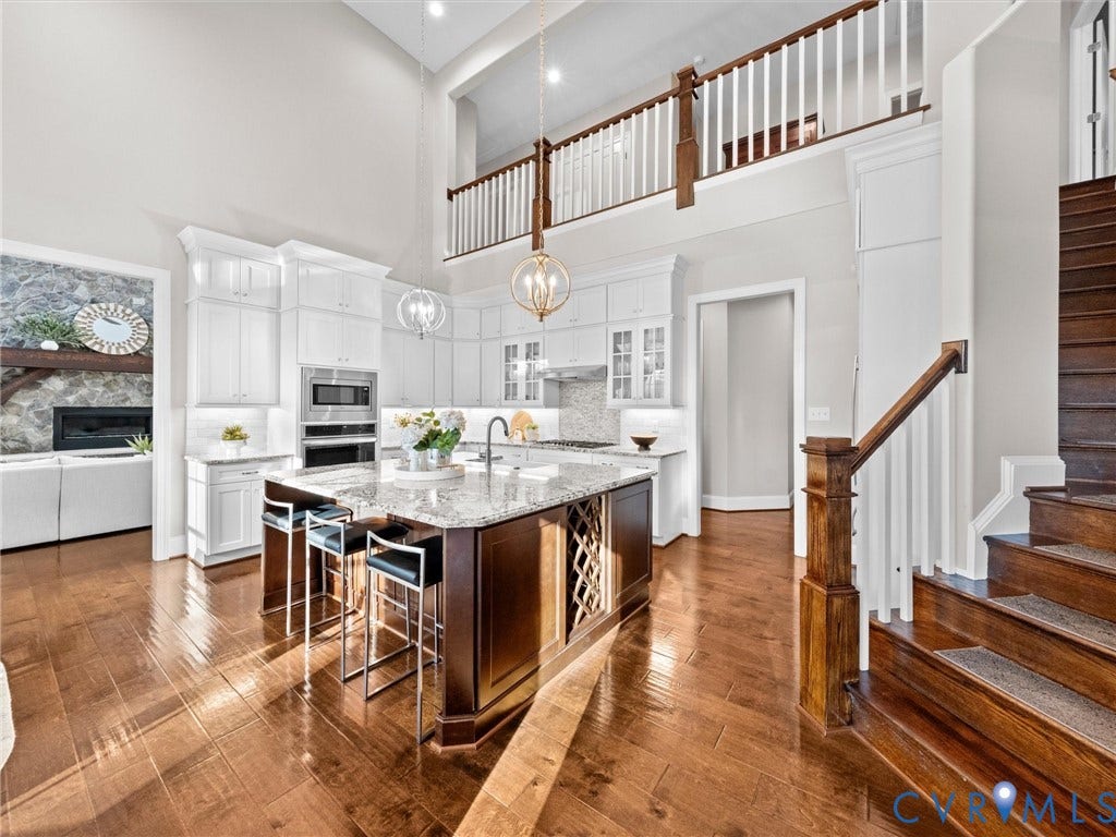 7750 Rock Cress Place, Chesterfield, VA 23120 High-ceiling kitchen featuring white shaker cabinetry, a center island with a built-in wine rack, wood-finish flooring, and a stone-clad fireplace surround