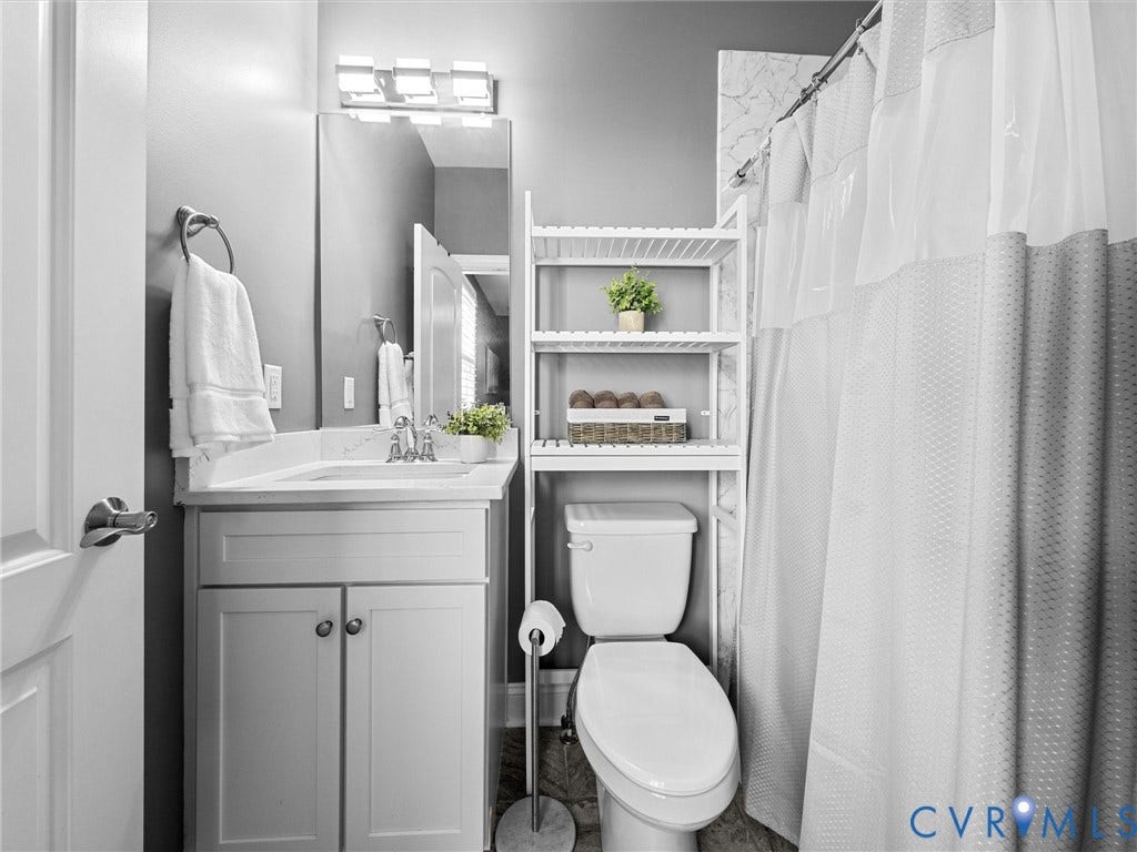 7750 Rock Cress Place, Chesterfield, VA 23120 Bathroom featuring a vanity with stone-finish countertop, integrated sink, wall-mounted light fixture, mirror, and a shower enclosure with tile surround