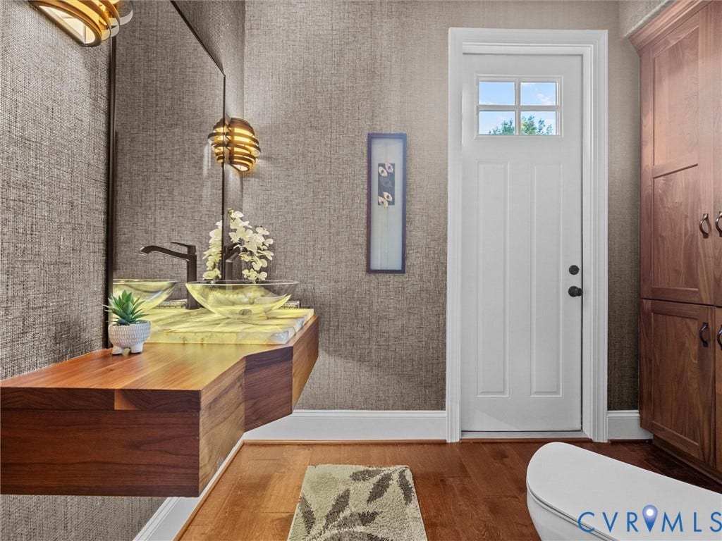 7750 Rock Cress Place, Chesterfield, VA 23120 Floating wood-finish vanity with a backlit stone countertop and glass vessel sink, matte black faucet, wall-mounted light fixtures, and floor-to-ceiling wood cabinetry