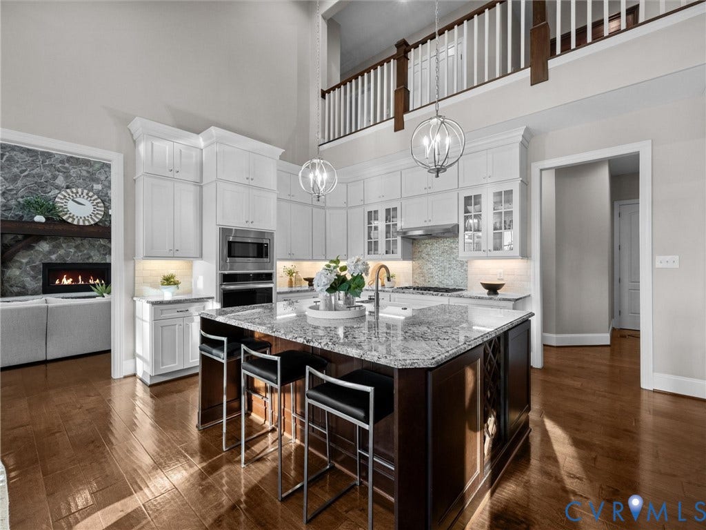 7750 Rock Cress Place, Chesterfield, VA 23120 Gourmet kitchen featuring white cabinetry, a center island with contrasting dark-finish base, stone-surface countertops, wood-finish flooring, and a two-story ceiling with a mezzanine overlook