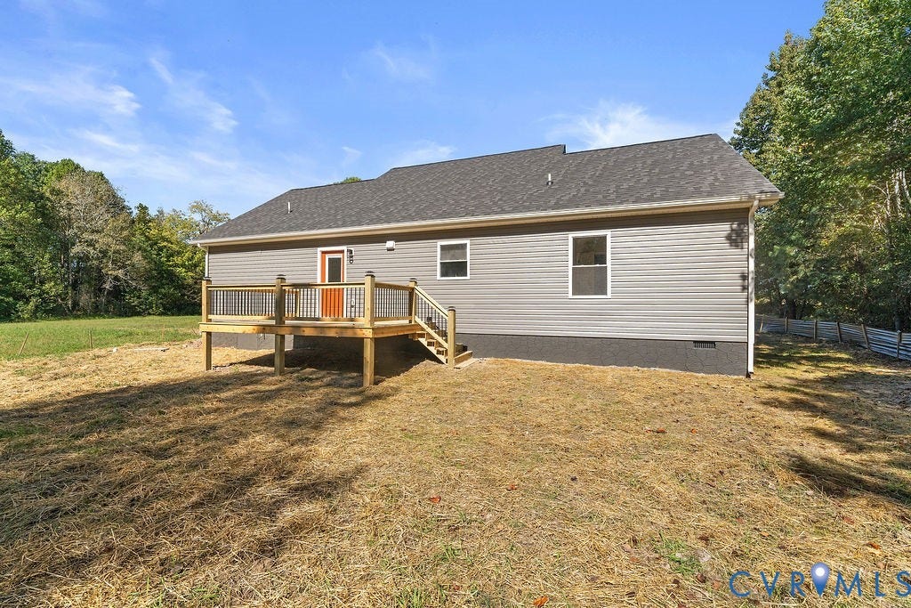 Rear exterior featuring a wood deck with railings, grey siding, a dark roof, and an orange door