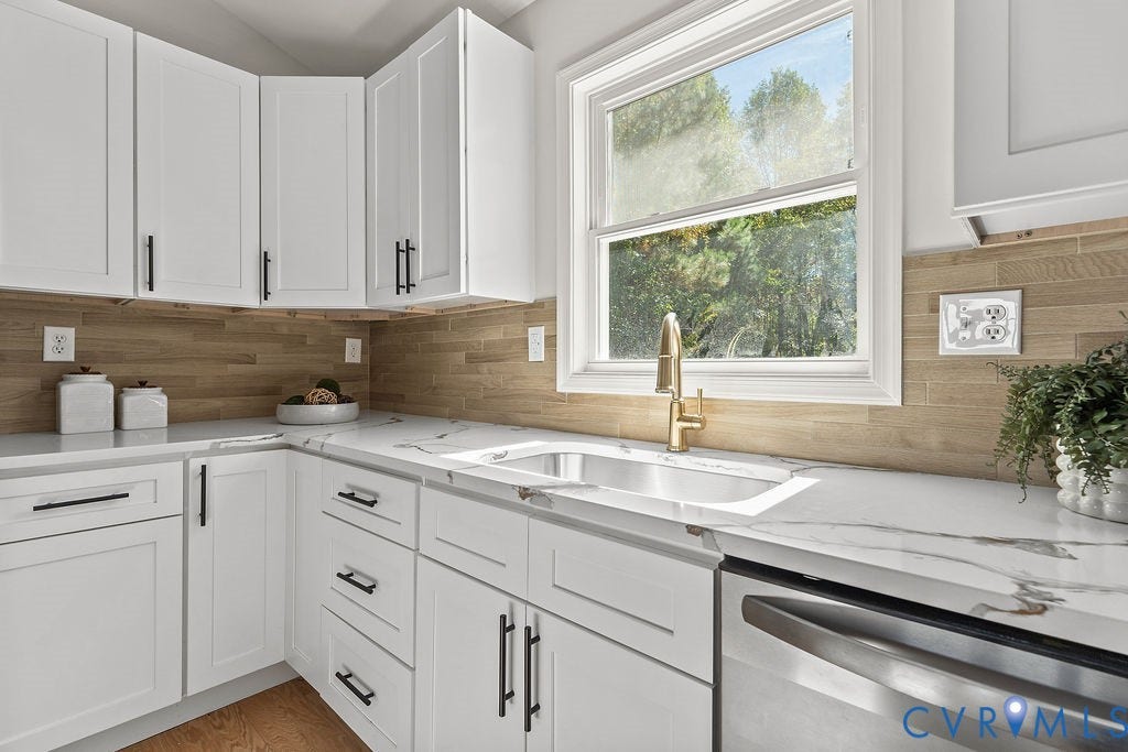White cabinetry with black hardware, wood-finish backsplash, undermount sink with gold-tone faucet, and stone countertops