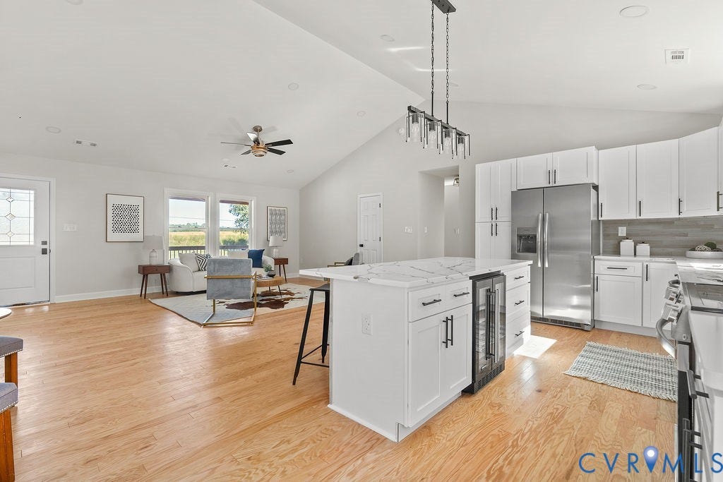 Open-concept living area with vaulted ceilings, wood-finish flooring, and a kitchen island featuring a beverage refrigerator