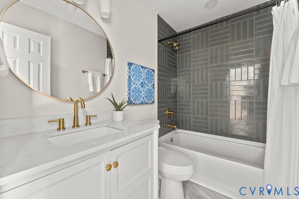 White vanity with paneling and gold hardware, rectangular undermount sink, gold-finish faucet, white countertop, and gold-framed round mirror