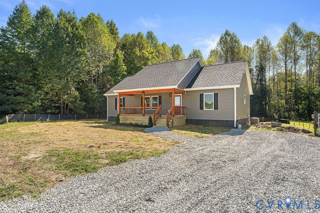 Charming cottage-style home featuring a brick and siding exterior with a covered front porch, gabled roofline with architectural shingles, and expansive gravel driveway