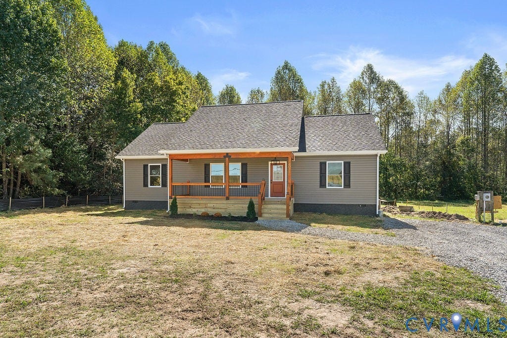 Siding exterior with a covered porch, wood-finish columns, a gravel driveway, and a natural tree line backdrop
