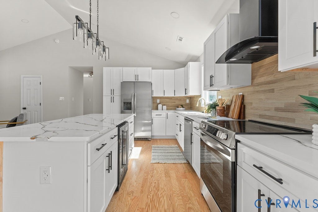 Kitchen featuring white shaker cabinetry, stainless steel appliances, a wood-finish backsplash, a large kitchen island with a beverage cooler, and vaulted ceilings
