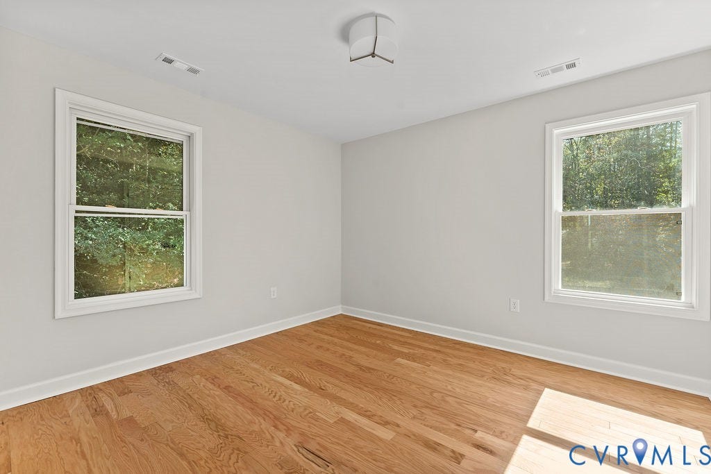 Light-filled interior featuring wood-finish flooring, two large windows, white trim, and a flush mount ceiling light