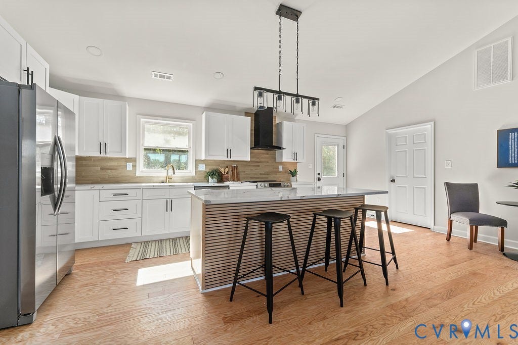 White cabinetry, stainless steel appliances, wood-finish flooring, island with a stone countertop, and vaulted ceiling