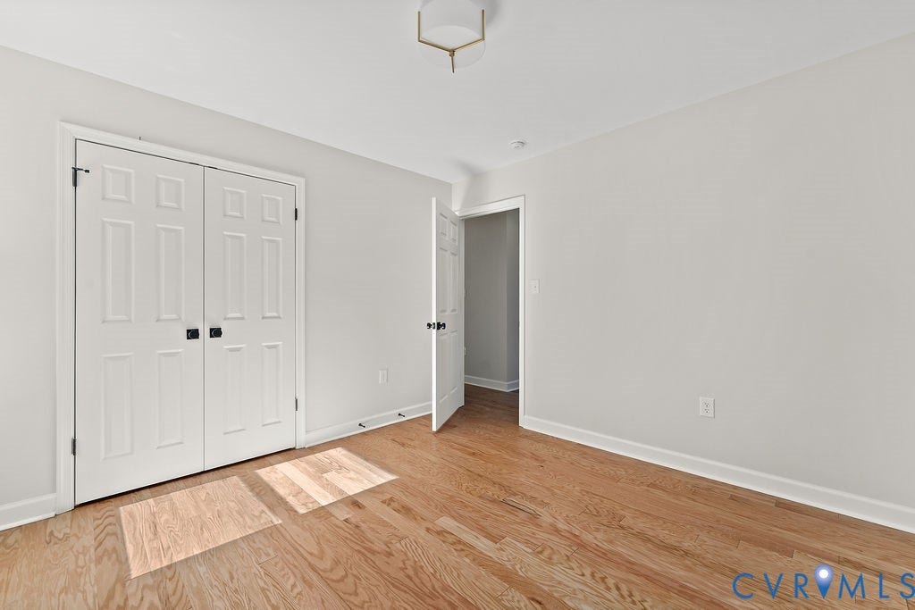 Wood-finish flooring, white walls, white trim, white paneled bifold closet doors with black hardware, and an overhead light fixture