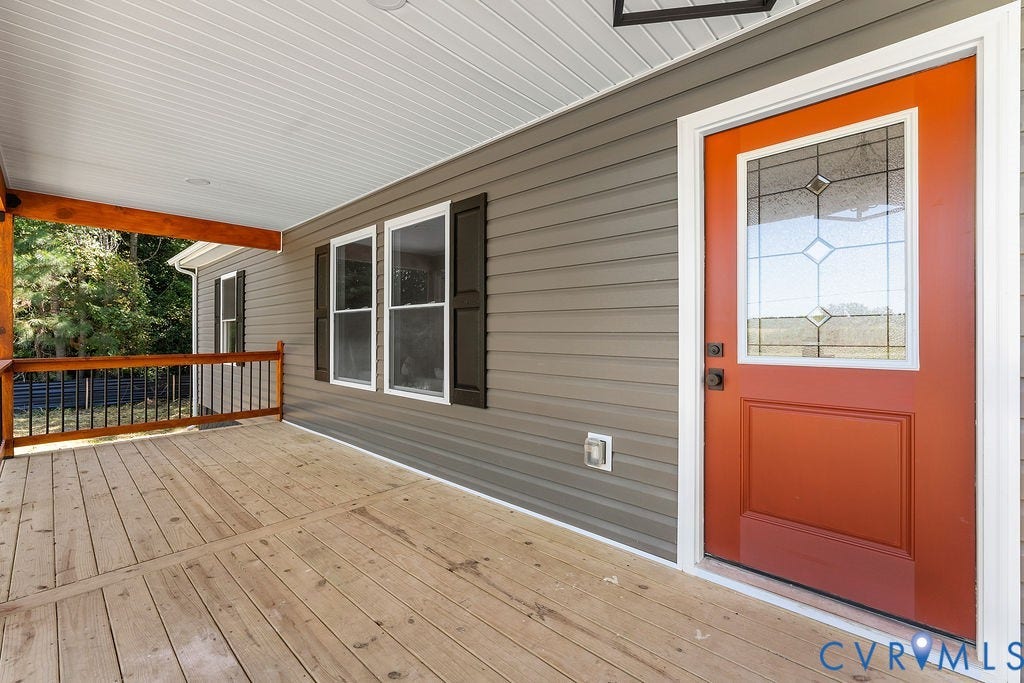 Covered wood-finish porch featuring a wood railing with black spindles, horizontal siding, and an orange front door with decorative glass