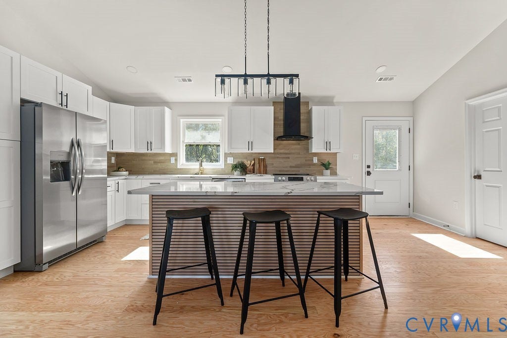 Modern kitchen featuring white cabinetry, a large kitchen island with a stone countertop, wood-finish flooring, and a stainless steel refrigerator