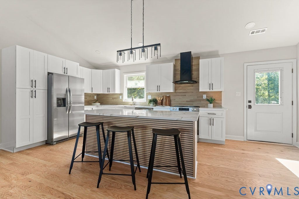 Kitchen featuring white cabinetry, stainless steel appliances, a center island with a wood-finish accent, light wood-finish flooring, and a modern range hood