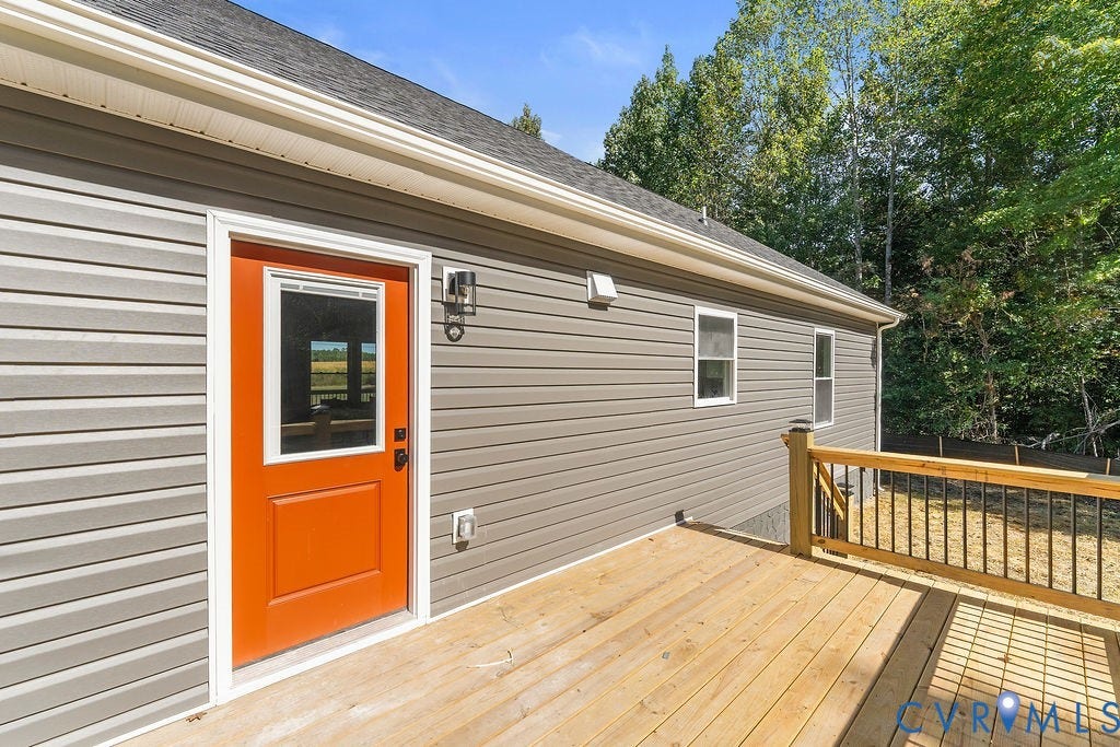 Expansive wood deck with a wood and wrought iron railing, gray horizontal siding, and a vibrant orange exterior door with a window pane