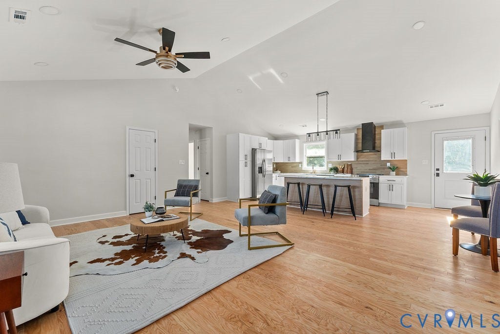 Vaulted ceiling with a ceiling fan, light wood-finish flooring, white kitchen cabinetry, kitchen island with seating, and a modern range hood