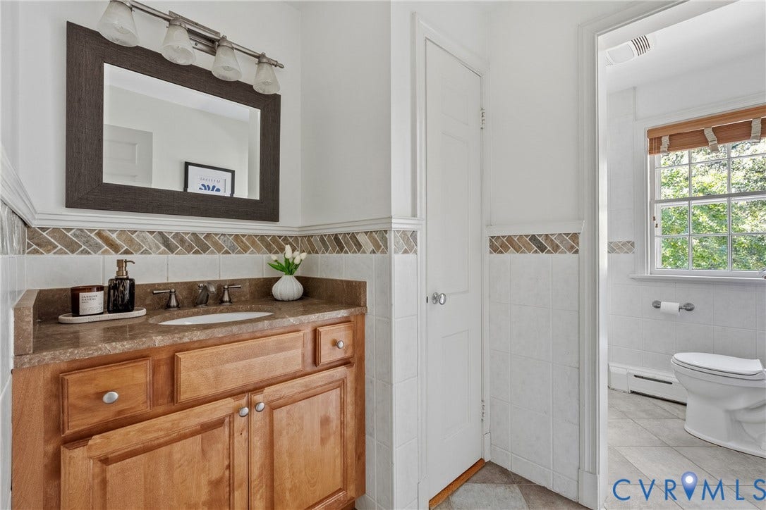 3700 Wakefield Road, Stratofrd Hills, Richmond, VA 23235 Bathroom featuring a wooden vanity, stone-finish countertop with an integrated sink, tri-light fixture, mirror with a dark frame, and decorative herringbone tile backsplash