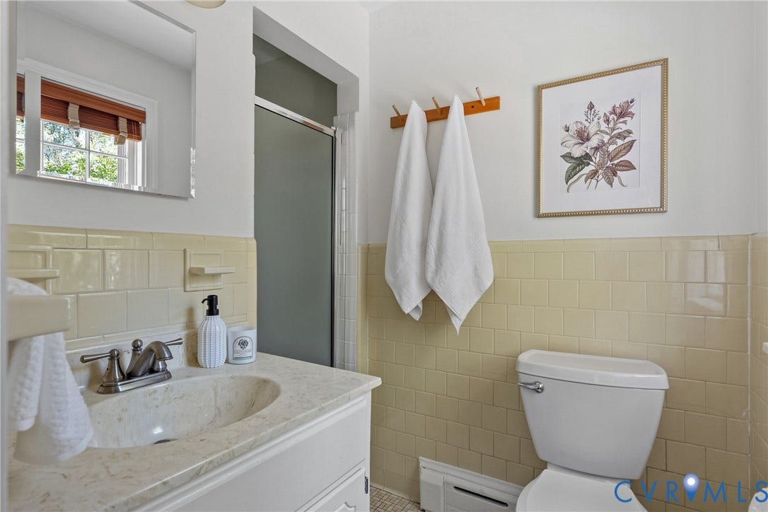 3700 Wakefield Road, Stratofrd Hills, Richmond, VA 23235 Bathroom featuring a vanity with stone-finish countertop, integrated oval basin, polished chrome faucet, partial-wall ceramic tile wainscoting, and a glass-enclosed shower