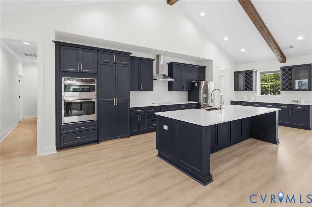 34356 Chinquapin Road, Waverly, VA 23890 Spacious kitchen featuring dark cabinetry, a large central island with a sink, white countertops, wood-finish flooring, and a vaulted ceiling with exposed beam