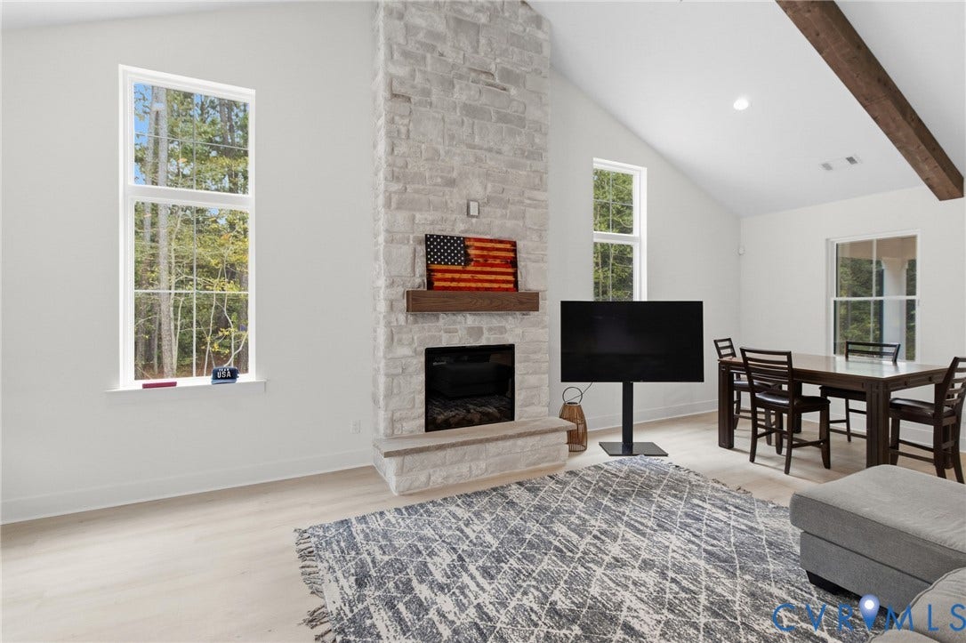 34356 Chinquapin Road, Waverly, VA 23890 Vaulted ceiling with exposed wood beam, stone-clad fireplace, light wood-finish flooring, and tall windows