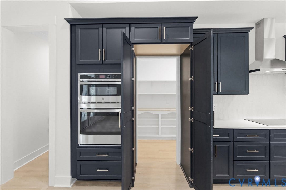 34356 Chinquapin Road, Waverly, VA 23890 Built-in double ovens, dark-toned cabinetry with crown molding, stainless steel range hood, light wood-finish flooring, and a white countertop