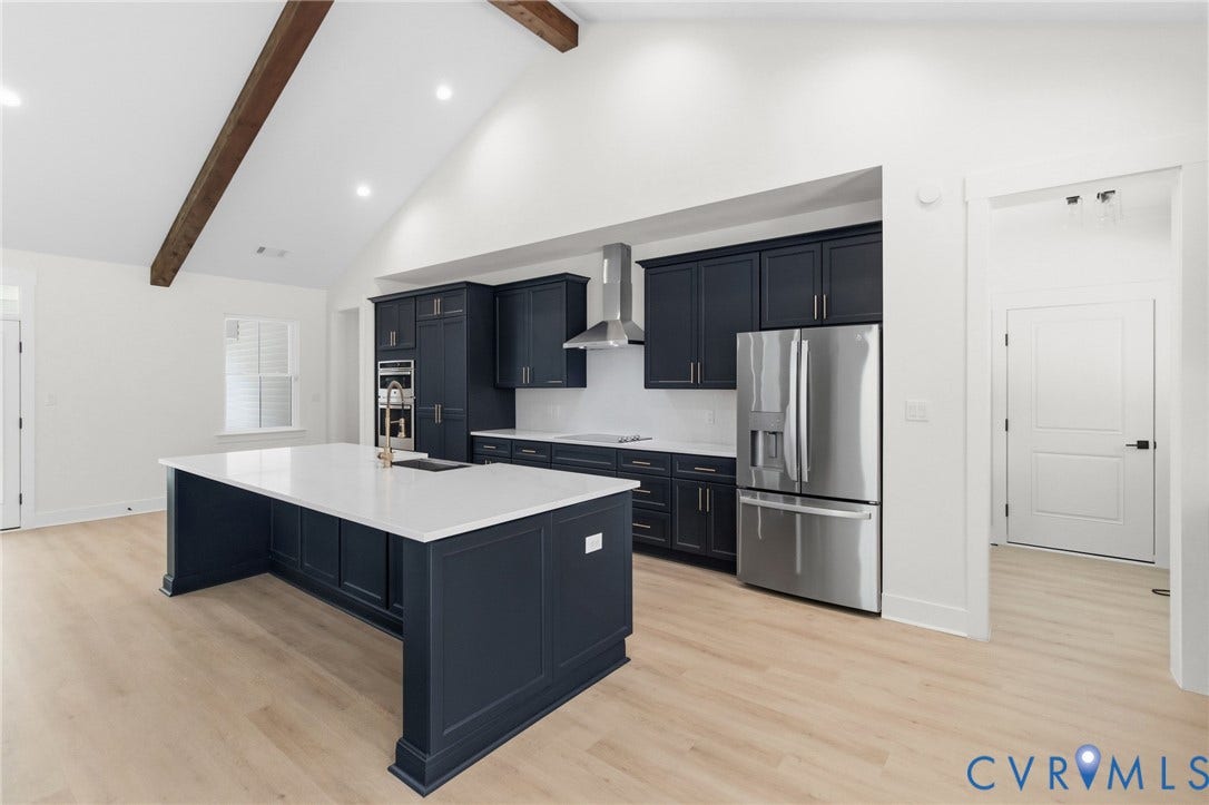 34356 Chinquapin Road, Waverly, VA 23890 Vaulted ceiling with exposed wood beam, light wood-finish flooring, dark cabinetry, stainless steel appliances, and a large central island with white countertop