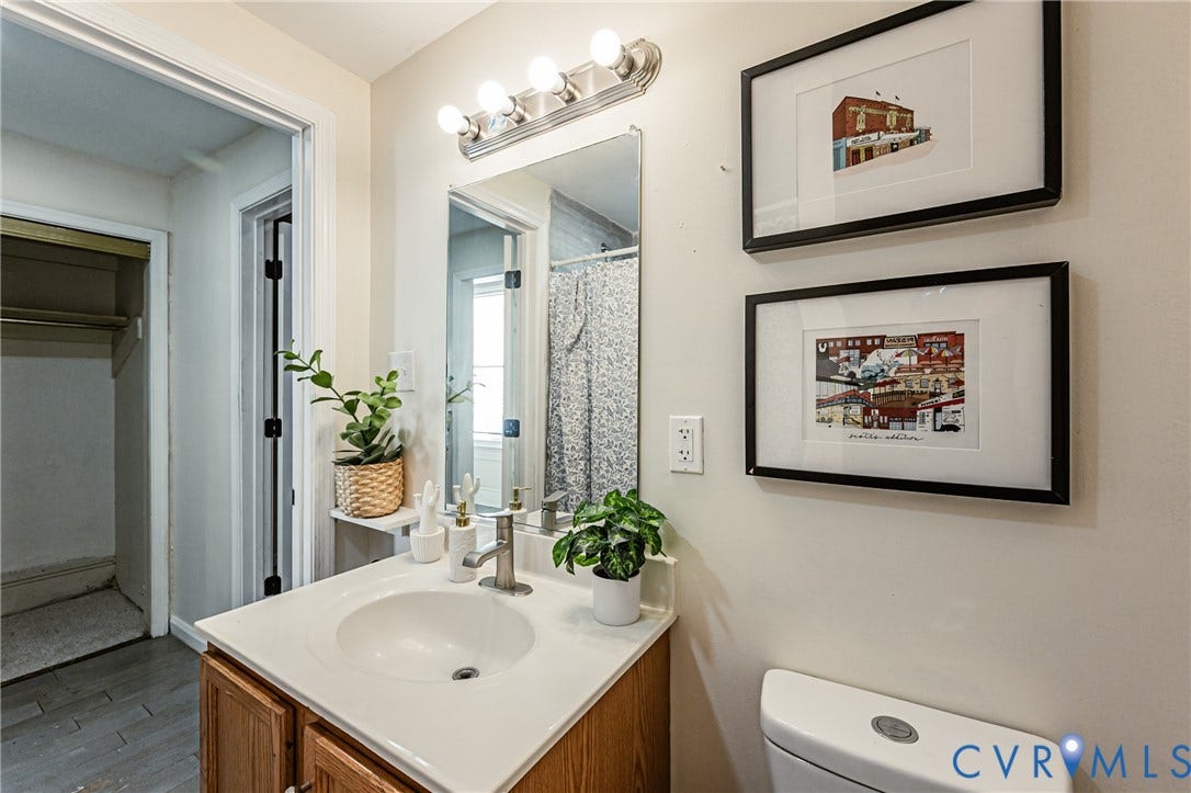 2011 Chicago Avenue, Richmond, VA 23224 Vanity featuring a white countertop with an integrated basin, wood-finish cabinetry, a polished metal faucet, and a four-bulb wall-mounted light fixture