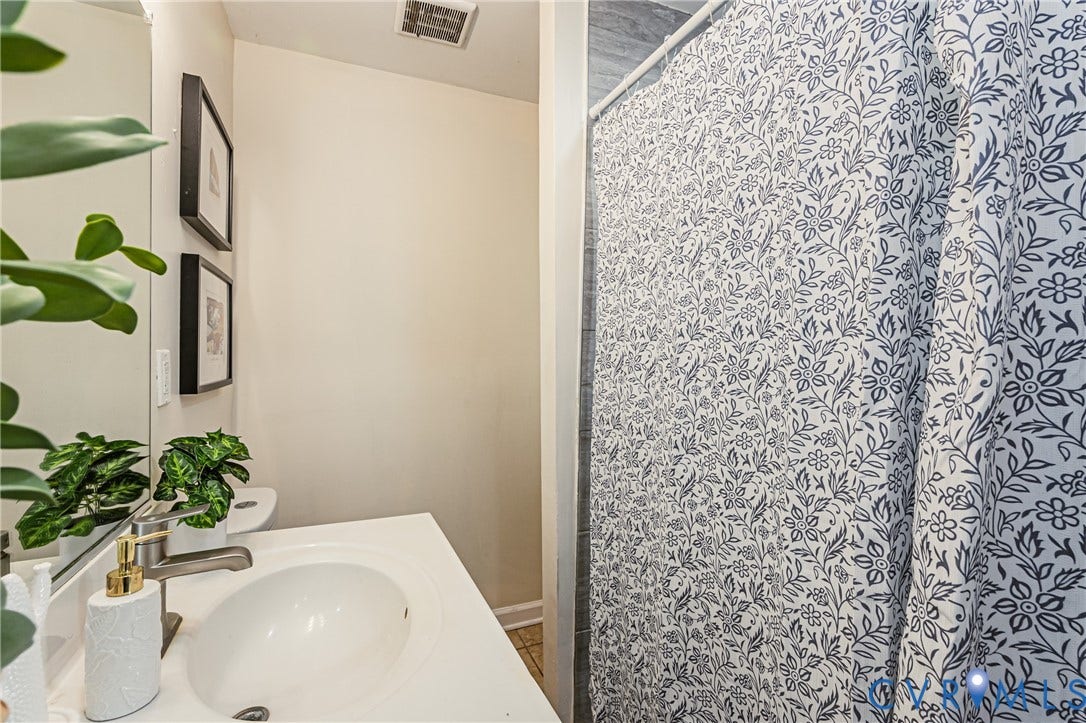 2011 Chicago Avenue, Richmond, VA 23224 Bathroom featuring a white vanity with a single-basin sink, brushed metal faucet, large wall-mounted mirror, and a shower area with grey-toned wall tiling