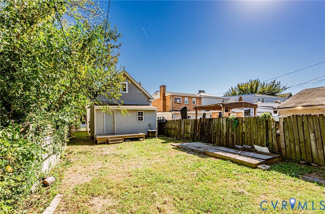 2011 Chicago Avenue, Richmond, VA 23224 Backyard area featuring a wooden deck, wood privacy fencing, mature trees, and an open grass lawn