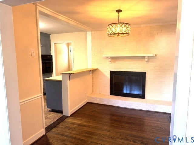 Hardwood flooring, painted brick fireplace with hearth, decorative light fixture, built-in shelf, and a pass-through counter with a wood top