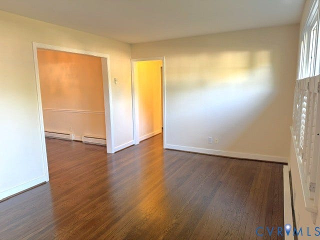 Spacious open-concept living area showcasing rich wood-finish flooring throughout, abundant natural light from large windows, and clean white trim detailing