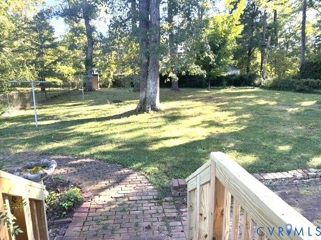 Expansive backyard oasis featuring mature shade trees, manicured lawn, brick hardscaping with planting beds, and deck access