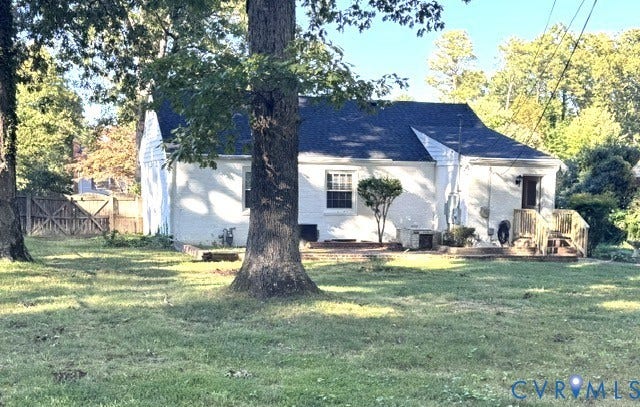 Expansive rear yard with mature trees, a white painted brick exterior, dark shingle roof, and a wood deck with stairs