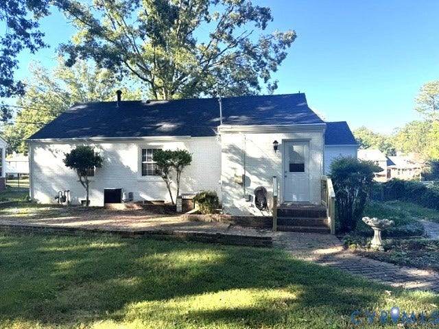 Charming cottage featuring a crisp white exterior with dark roof accents, brick foundation detailing, and a covered entry portico