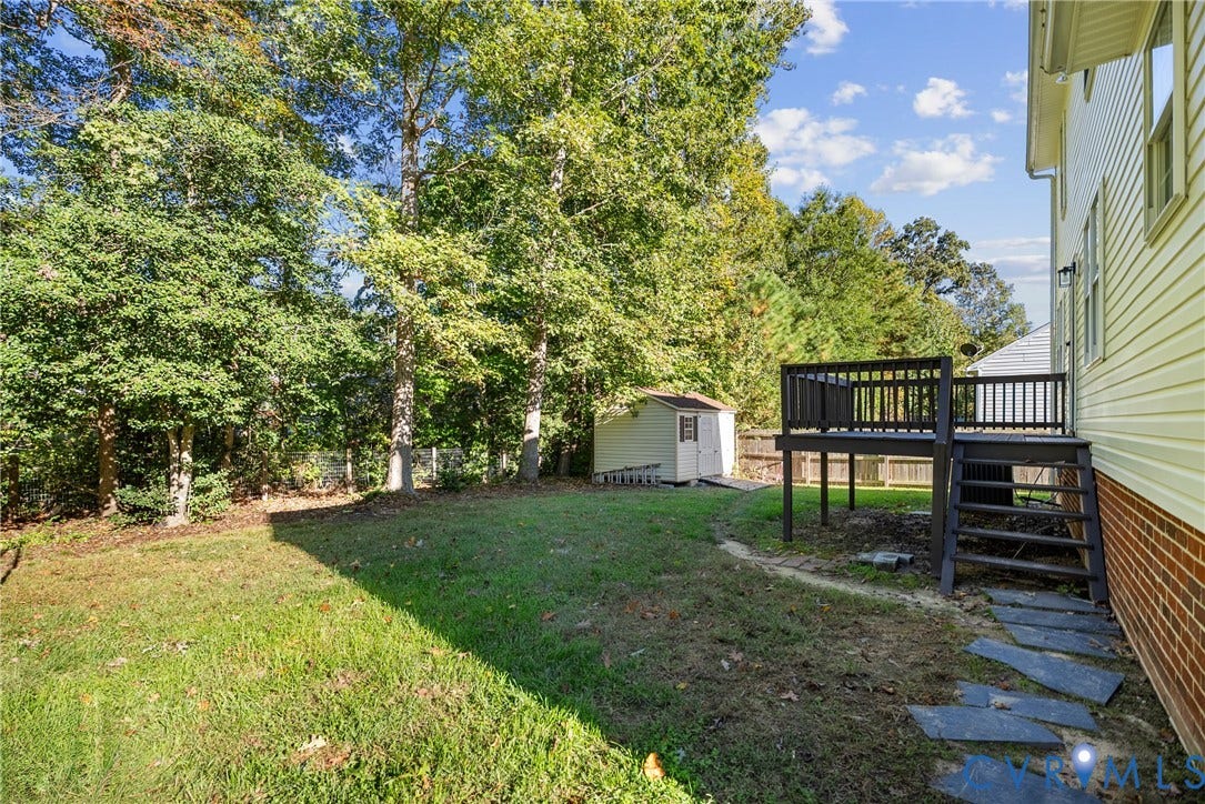 11512 Wiltstaff Drive, Midlothian, VA 23112 Rear exterior featuring a raised wood deck with stair access, stone paver pathway, detached storage structure, and tree-lined perimeter