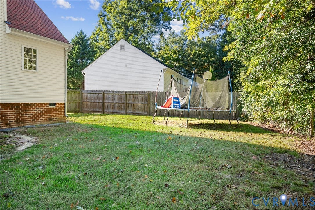 11512 Wiltstaff Drive, Midlothian, VA 23112 Rear exterior featuring light-colored siding, a brick foundation, and a fenced backyard with mature trees