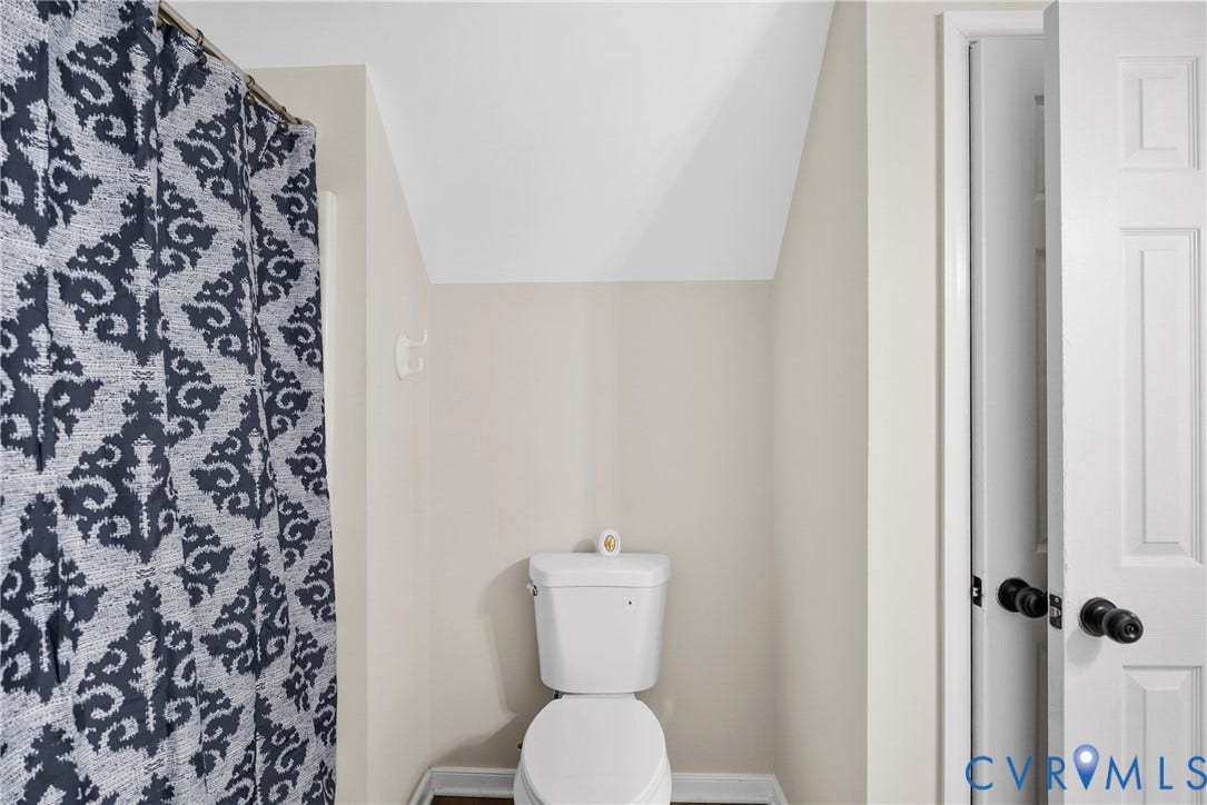 11512 Wiltstaff Drive, Midlothian, VA 23112 Bathroom featuring a white two-piece toilet, angled ceiling, and a paneled door with matte black hardware
