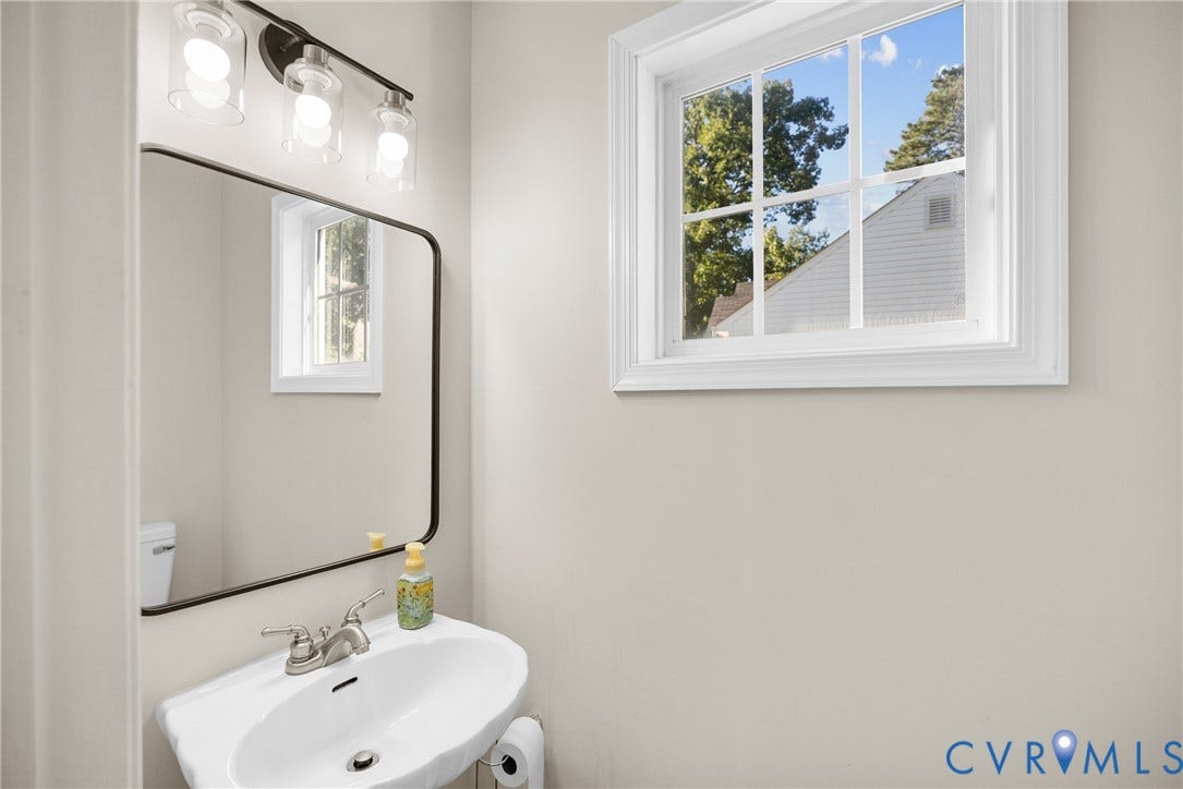 11512 Wiltstaff Drive, Midlothian, VA 23112 Wall-mounted white pedestal sink with polished chrome faucet, rectangular mirror with thin black frame, and three-light vanity fixture featuring clear glass shades and decorative bulbs
