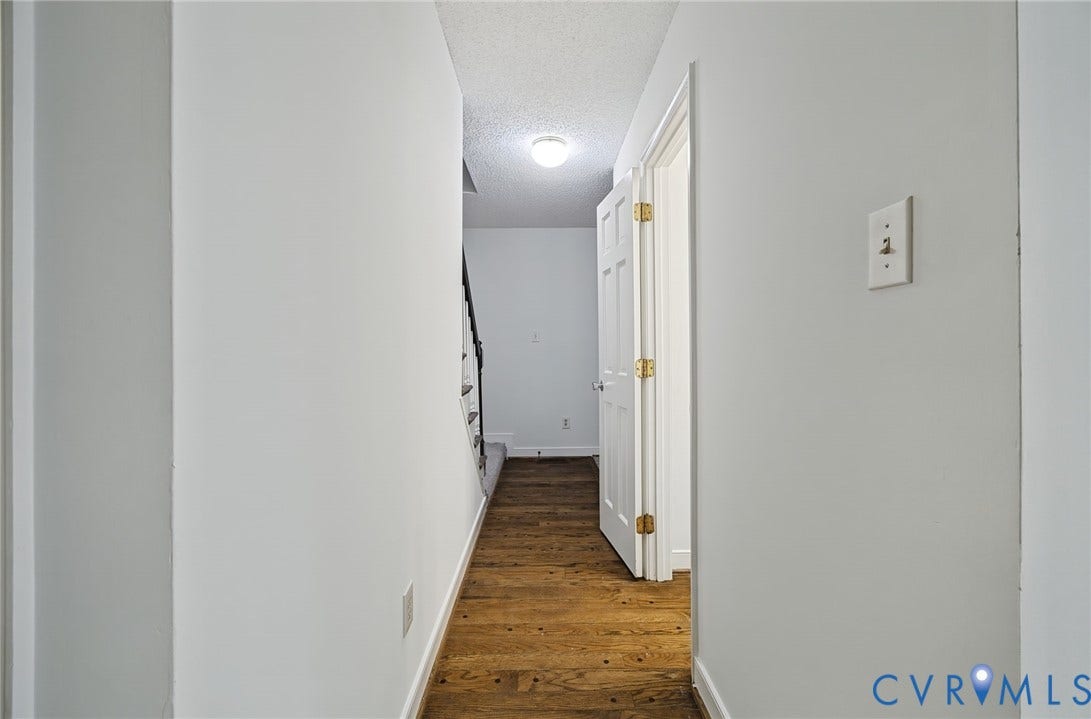 Hallway featuring wood-finish flooring, a six-panel door with gold-tone hardware, and a ceiling-mounted flush light fixture