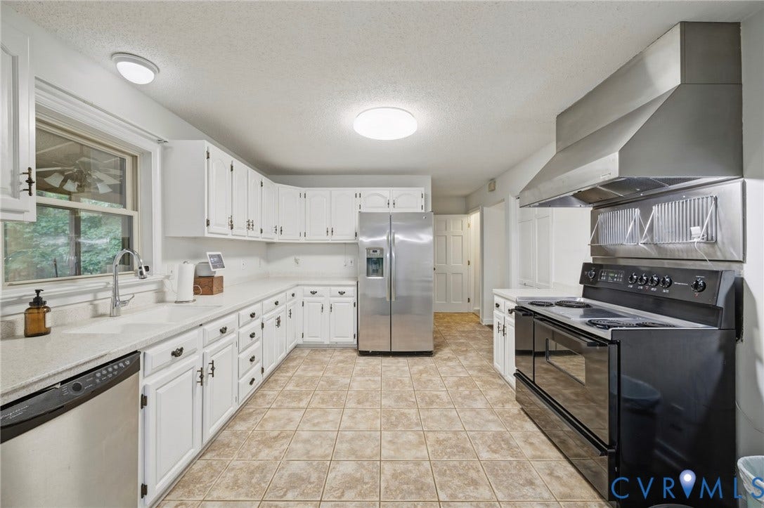 Kitchen featuring white cabinetry, light-toned solid surface countertops, stainless steel appliances, a professional-style range hood, and tile flooring