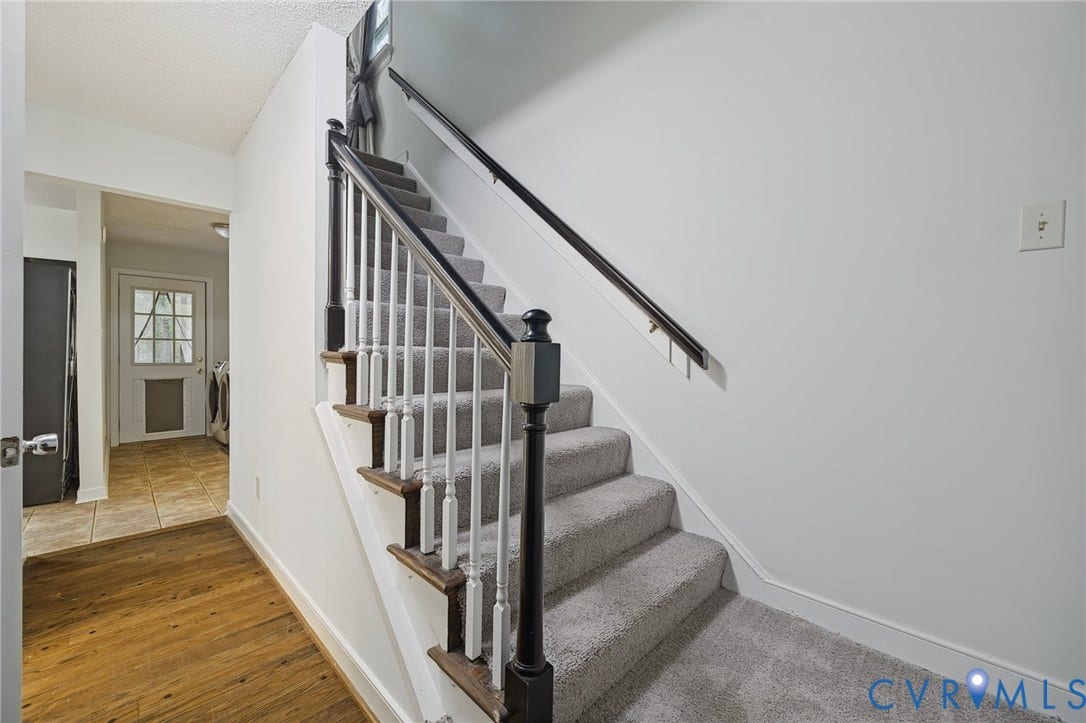 Staircase featuring a high-contrast black handrail, white balusters, and wood-finish treads, complemented by neutral carpeting