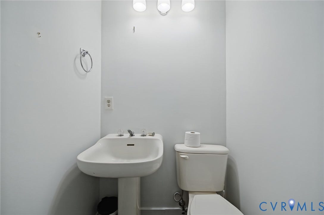 Wall-mounted three-light fixture, pedestal sink with dual-handle faucet, circular towel ring, and standard-height toilet