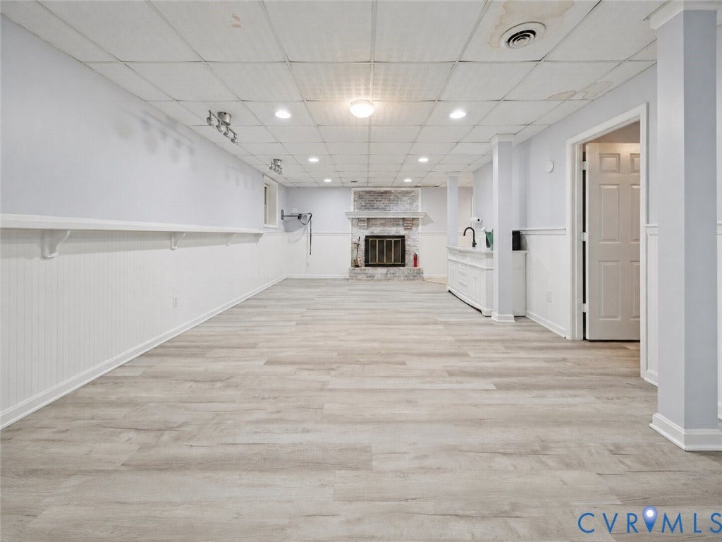 Finished space featuring wood-finish flooring, white beadboard wainscoting, a stone-surround fireplace, built-in cabinetry with a sink, and recessed lighting
Virtually edited