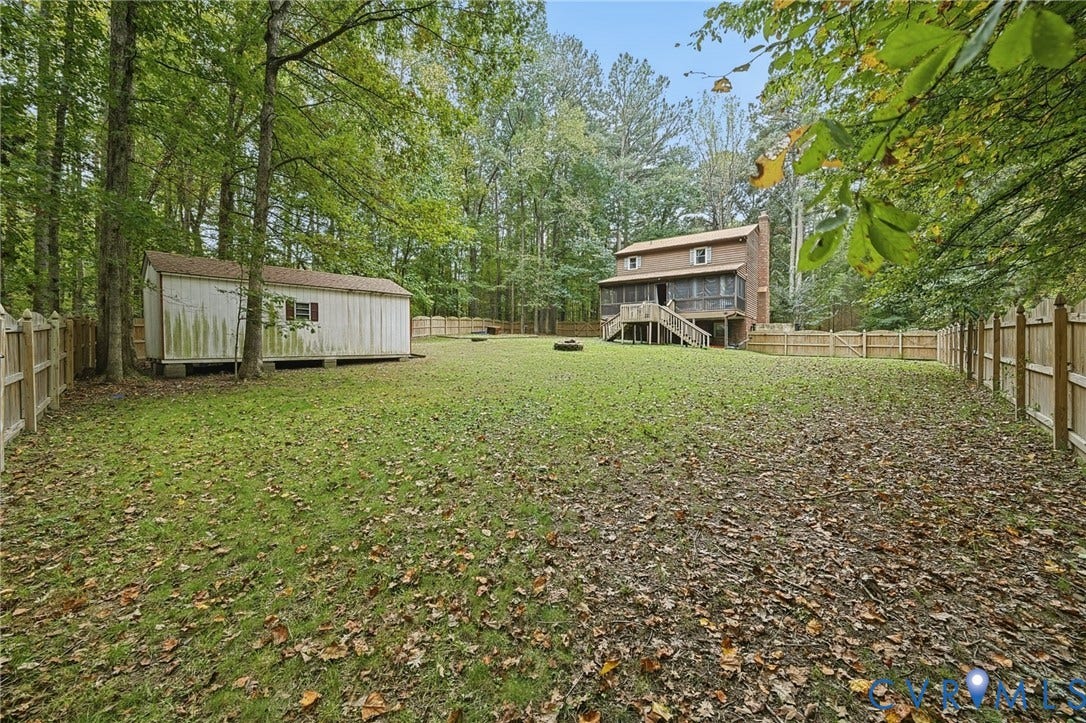 Expansive backyard featuring a fenced perimeter, detached storage shed, elevated rear deck, and established tree canopy