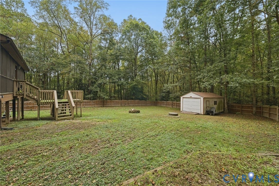 Expansive backyard featuring a wood deck, perimeter wood fencing, a detached storage shed, and mature trees