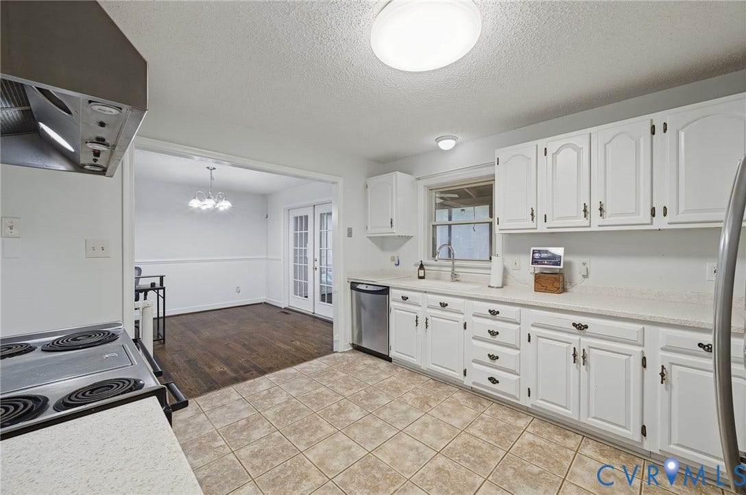 Kitchen featuring white cabinetry, solid-surface countertops, stainless steel dishwasher, and ceramic tile flooring